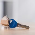 key with toy house trinket on stack of holden and silver coins on wooden table