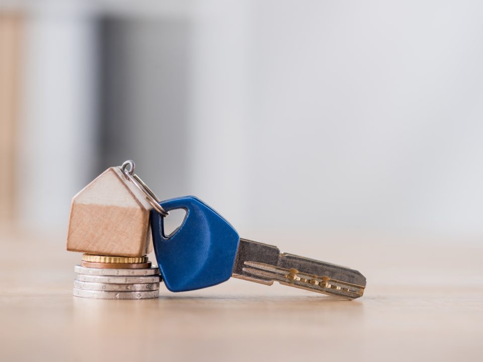 key with toy house trinket on stack of holden and silver coins on wooden table